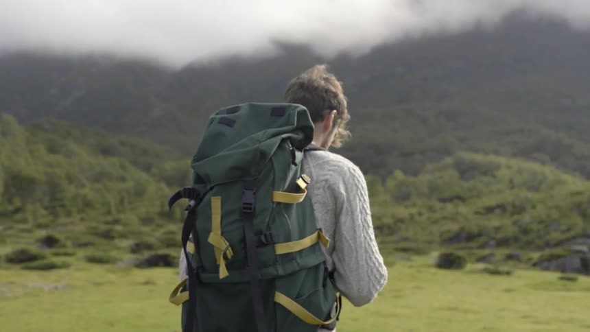 A dedicated backpacker climbs a steep green hill toward a remote wilderness summit.