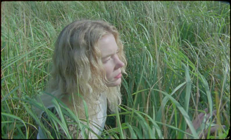 Young blonde woman sits on a field of tall grass