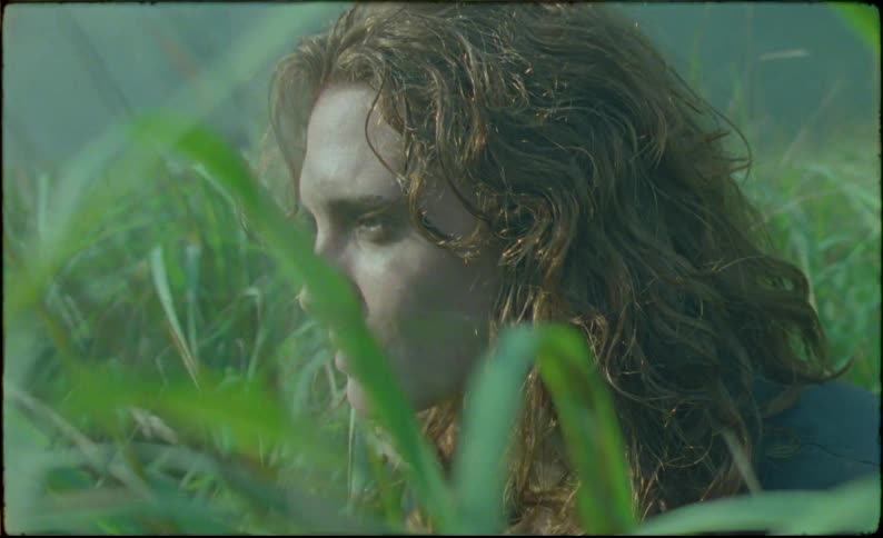 Redheaded woman crouching in grass looks around and removes her over top before standing