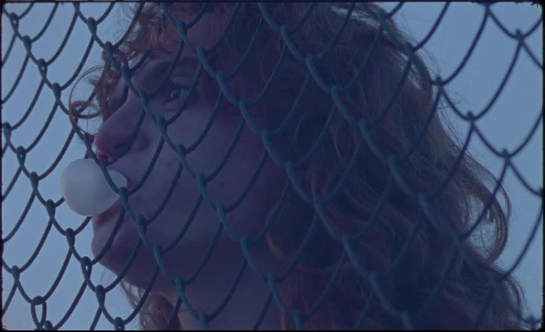 A person standing behind a netted fence blowing gum