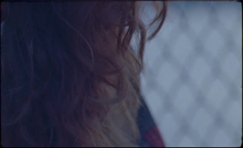 Redheaded woman eats outdoors near chain link fence