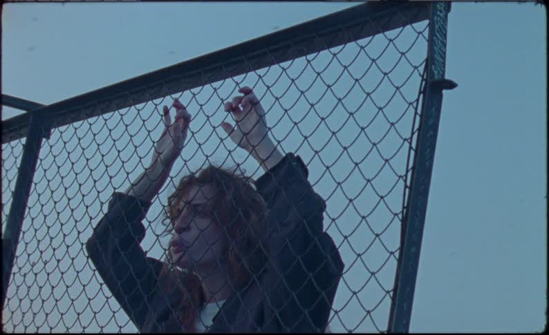 Young woman reclined on a chain link fence chewing bubblegum