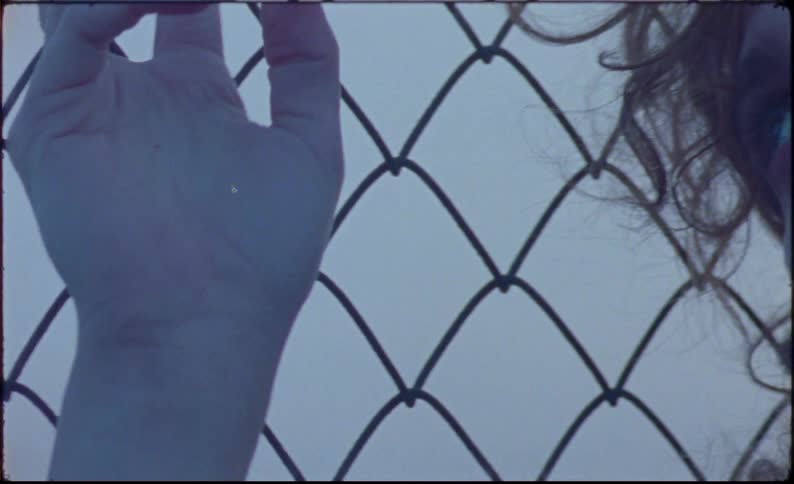 Person leans against a chain link fence on an overcast day