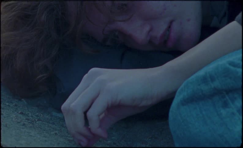 Person in fetal position on concrete picks at rocks looking forlorn