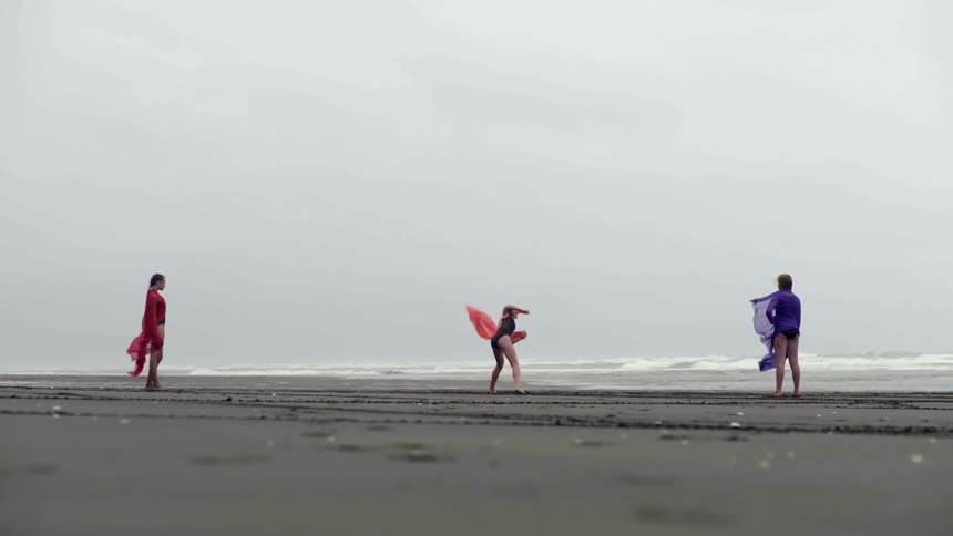 Three artistic performers prepare an outdoor collaborative dance project on a desolate beach.