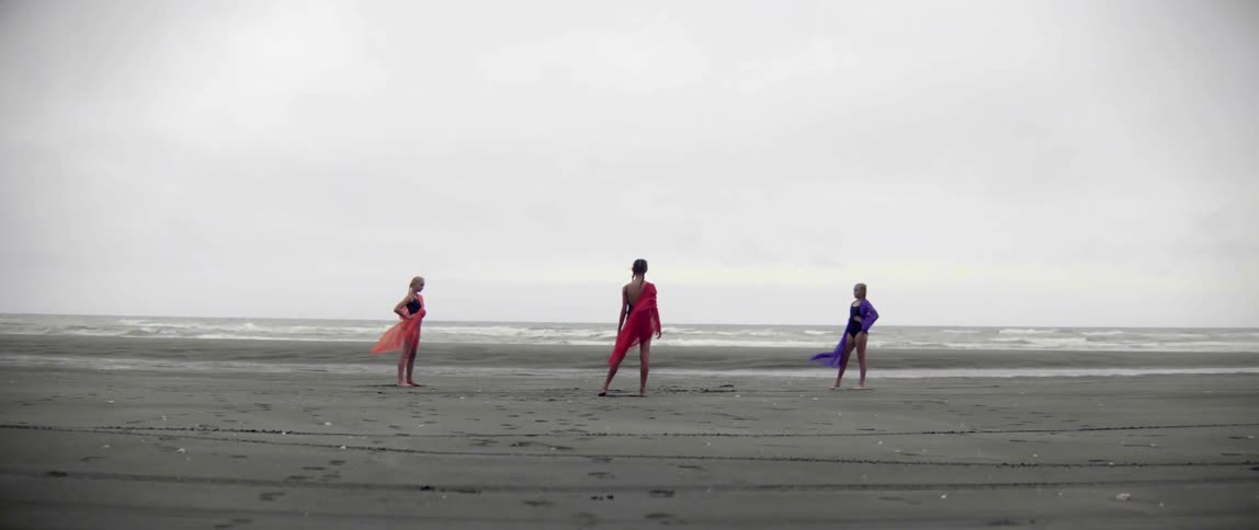 Three young women converge on a beach holding different colored fabrics