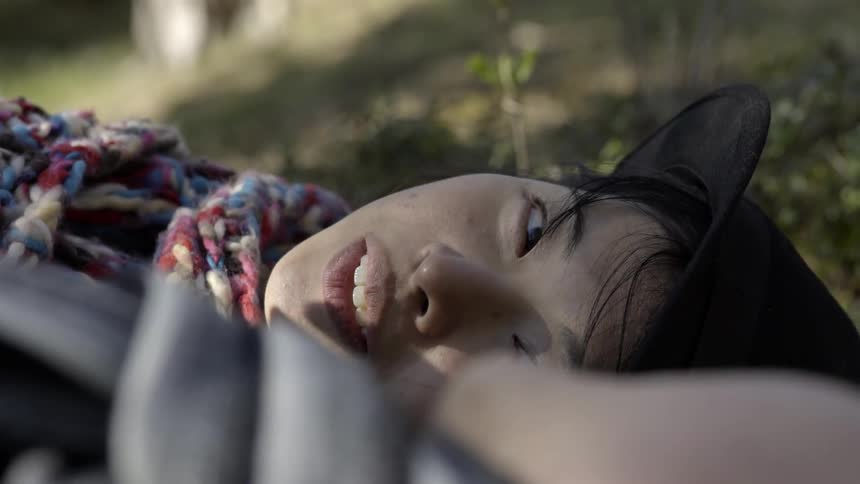 a woman relaxing outdoors while talking to someone off-camera in sunlight.