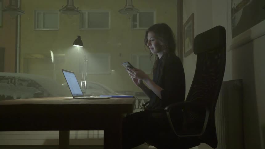 A woman sitting at a desk in a dark room working on laptop