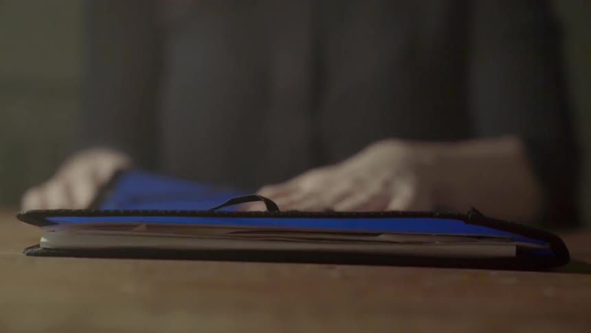 A woman slams shut a blue portfolio containing important papers on a wooden table.