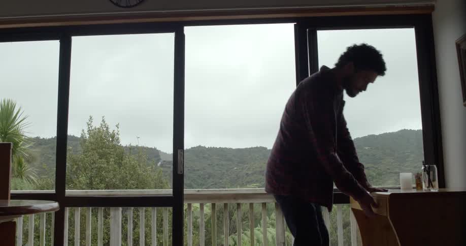 Man stands in house next to large windows and suddenly goes to open a drawer