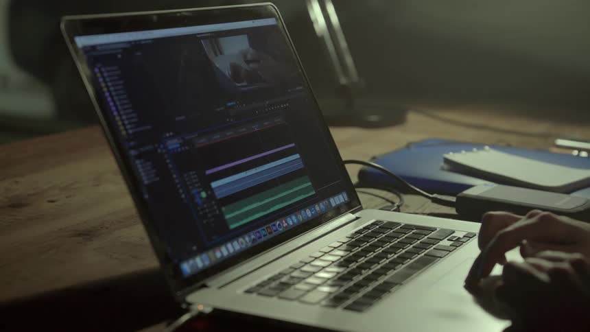 A creative professional works on a laptop reviewing and editing digital video content indoors.