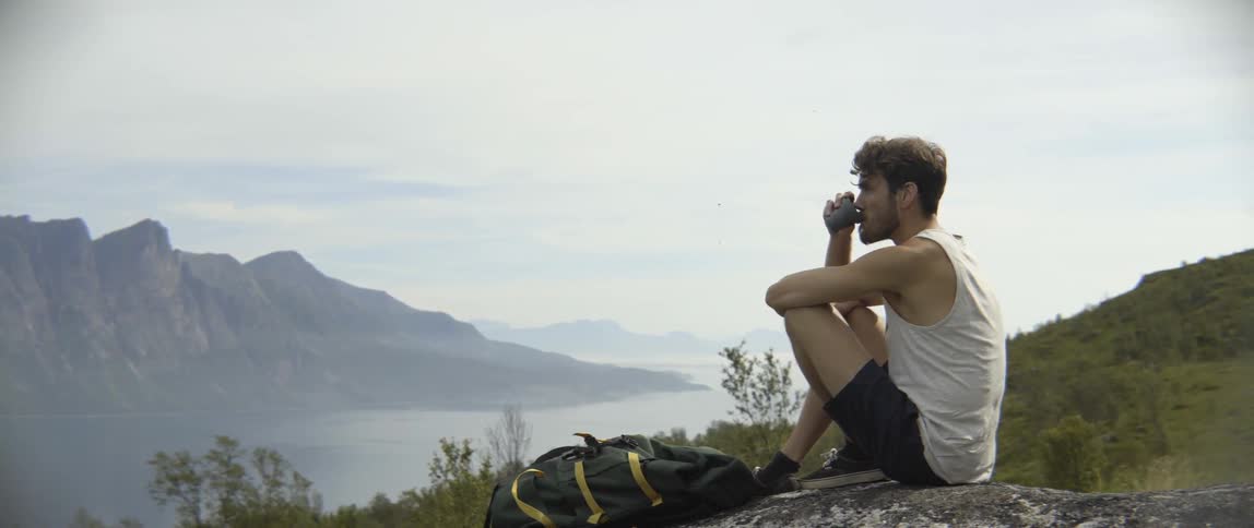 A satisfied traveler enjoys a warm beverage while admiring a stunning lake overlook outdoors.