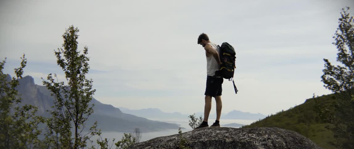 A hiker stands up with his backpack while overlooking a valley