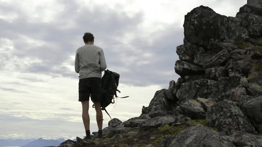 A young takes off his backpack and sits down on a rocky peak