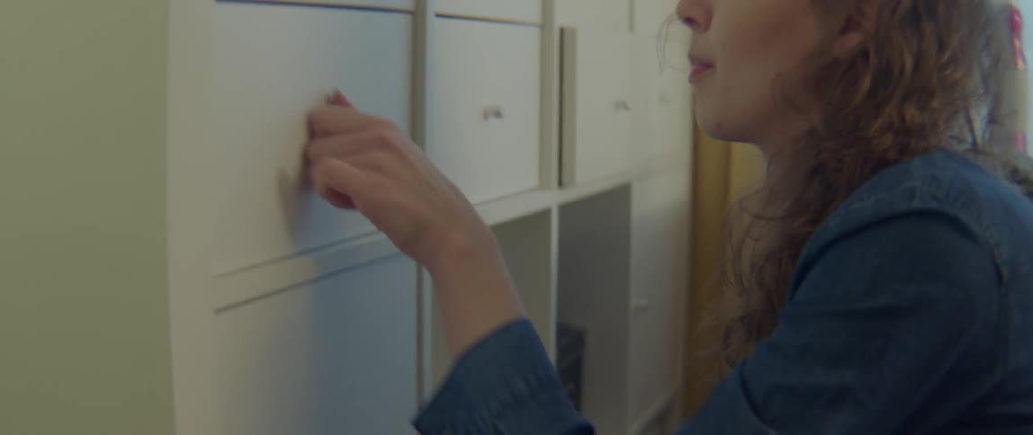 A woman frantically rummages through a cardboard box and cupboard
