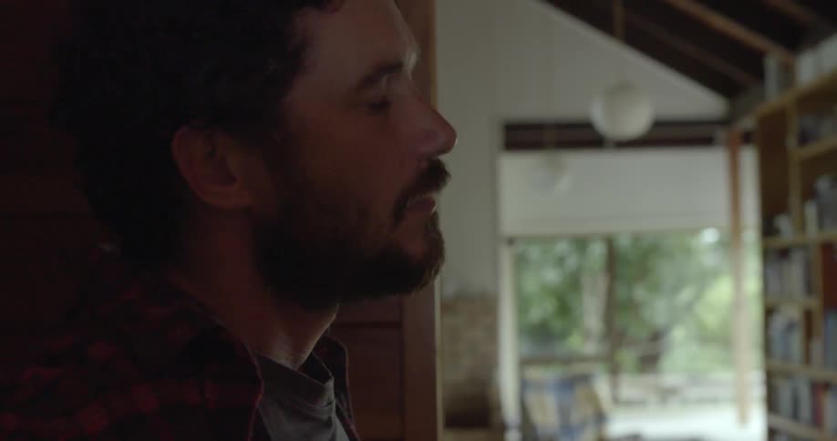 a bearded person observing their surroundings inside a bright domestic space.