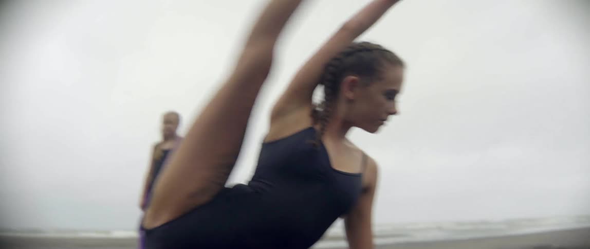 Woman getting dirty while practicing her acrobatics on a beach on a cloudy day