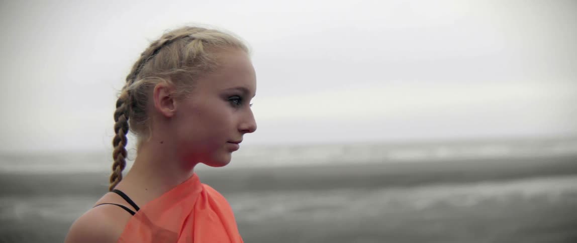 A young woman stands as her hair blows in the breeze on the shoreline