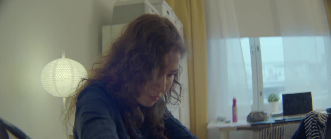A woman sitting in a room notices she's missing something and begins searching for it
