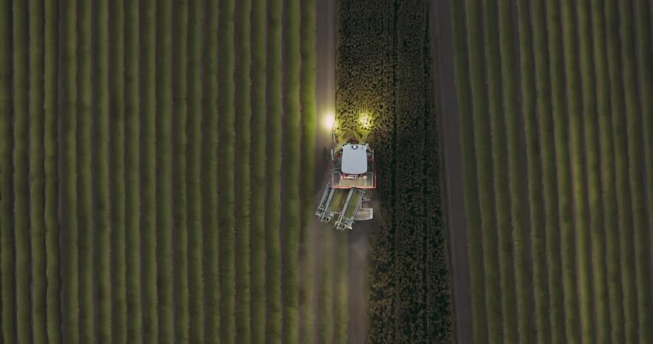 Headlights glow on a tractor plowing a farm field at night
