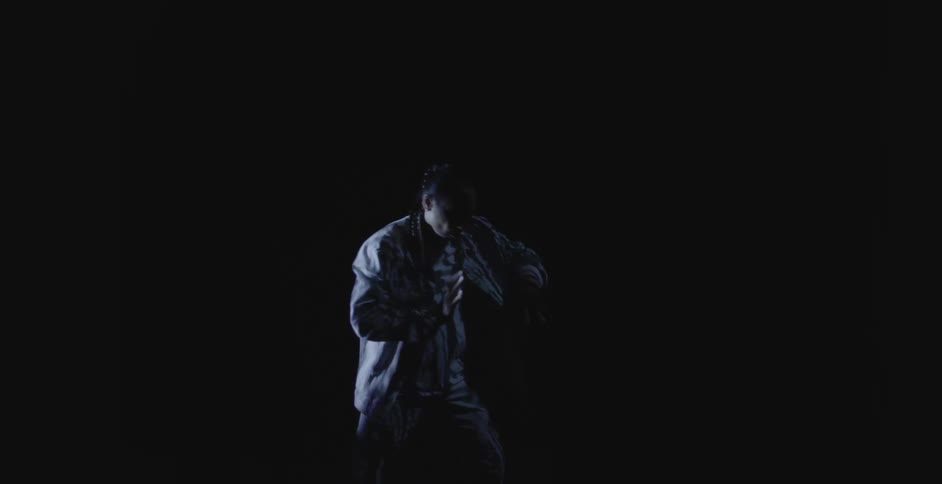 Man wearing loose fitting clothes moves through flowing routine in dark area