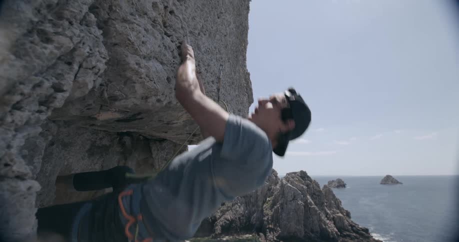 Man climbs a rock wall in the cliffs next to the ocean