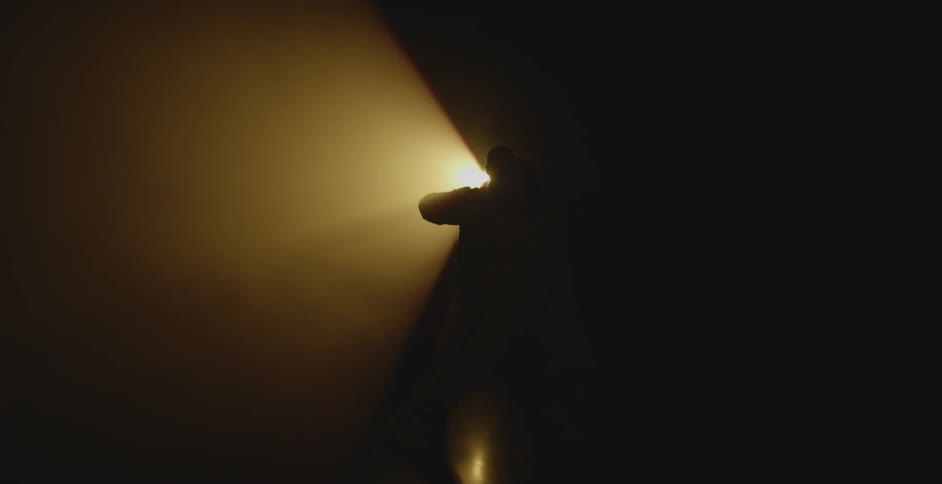 Silhouettes of two people dancing in a dark room illuminated by a beam of light