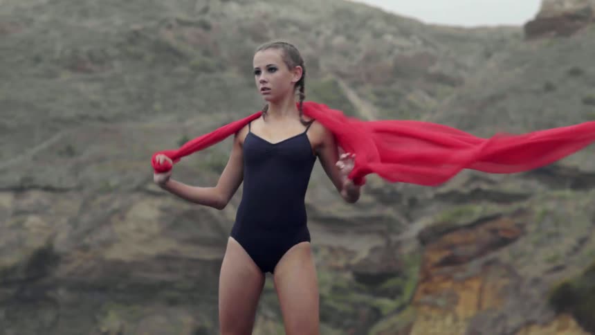 An expressive young artist stands proudly on a stormy coastline with her performance fabric.