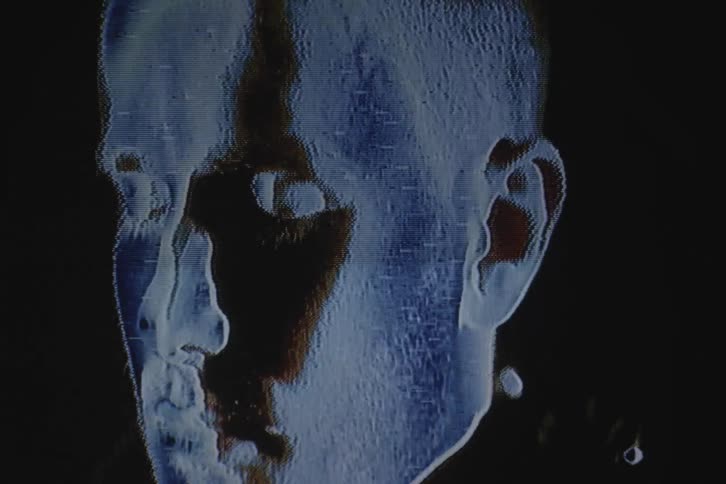 Distorted opening and then tight focus on a face against a dark backgroundbut the lighting is dark and eerie as the light moves in a wave across the face as the man opens his eyes
