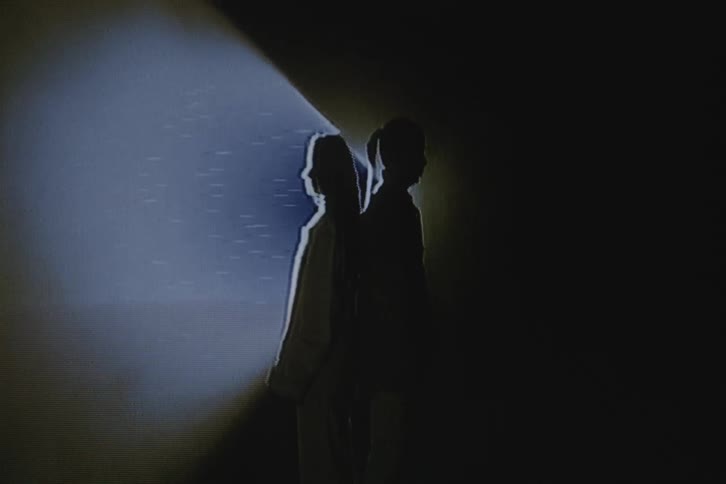 Two people are standing back to back while a spotlight shines on them