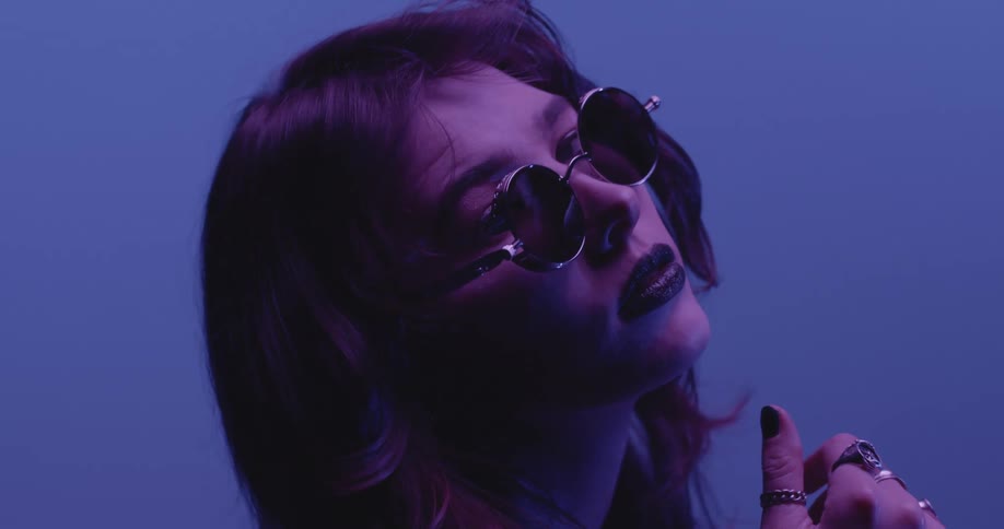 A woman wearing sunglasses poses under purple lighting