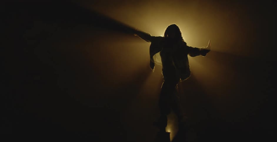 A woman extends her arms while dancing in front of a bright spotlight