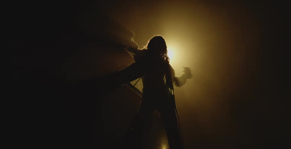 Silhouette of a person dancing in a dark room lit by a spotlight