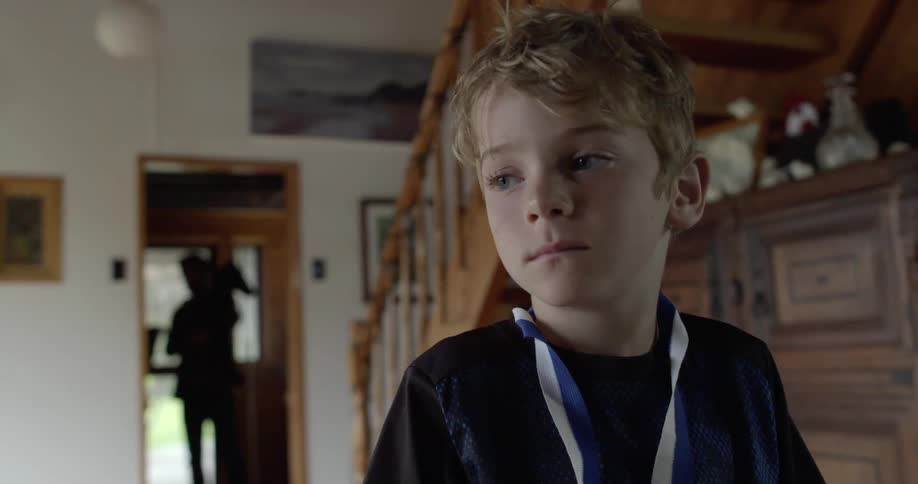 Young boy with a medal around his neck stands in living room