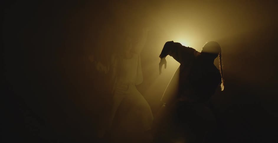 Two people dance in front of the spotlight in the dark