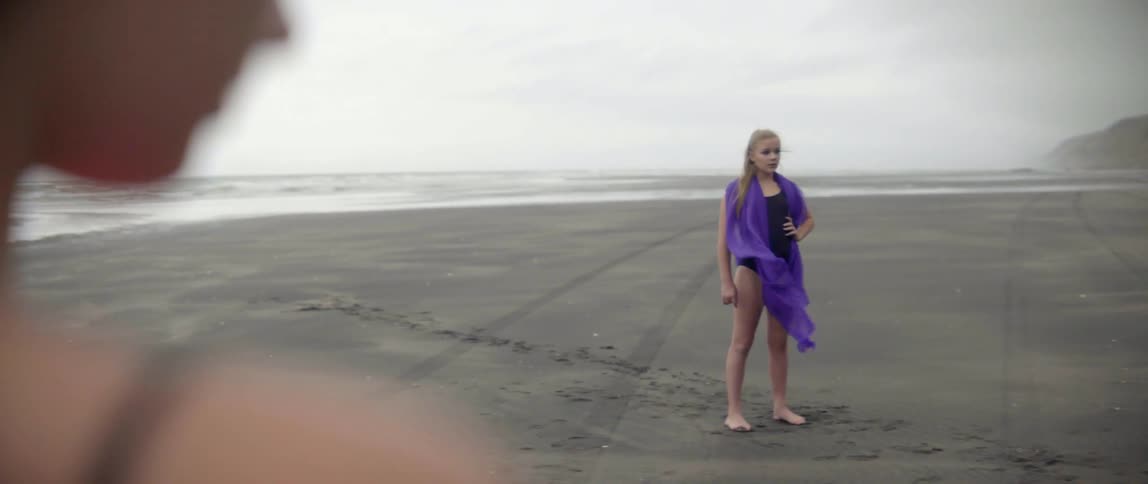 A girl is standing on the beach with a purple scarf on her shoulders