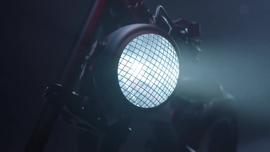 A round retro headlight on a motorcycle glowing at night