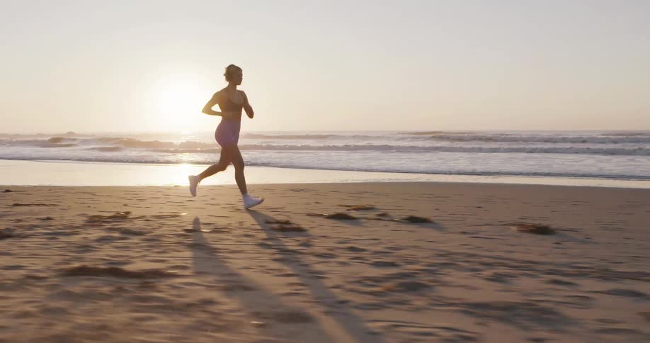 A young blonde woman runs along the beach at sunrise