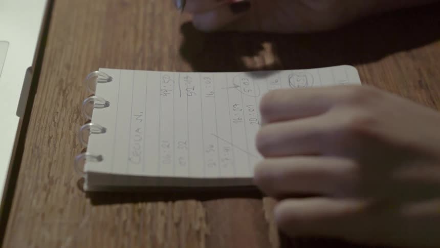 A person takes detailed notes in a spiral notebook during a quiet creative session.