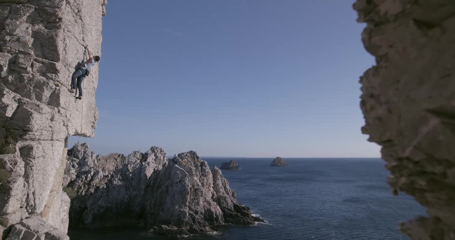 Man climbs a rock wall in the cliffs next to the ocean