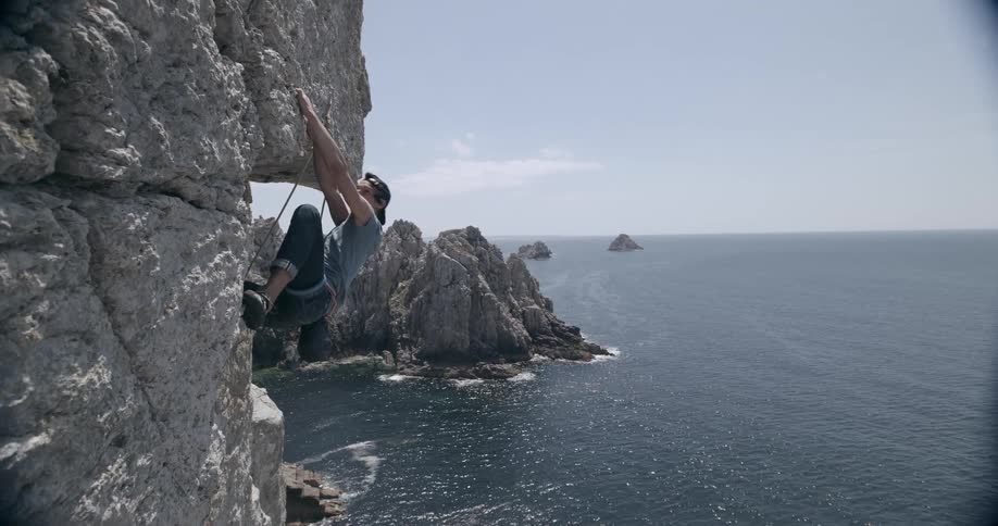 Young adult male rock climber scales a coastal rock cliff over the ocean