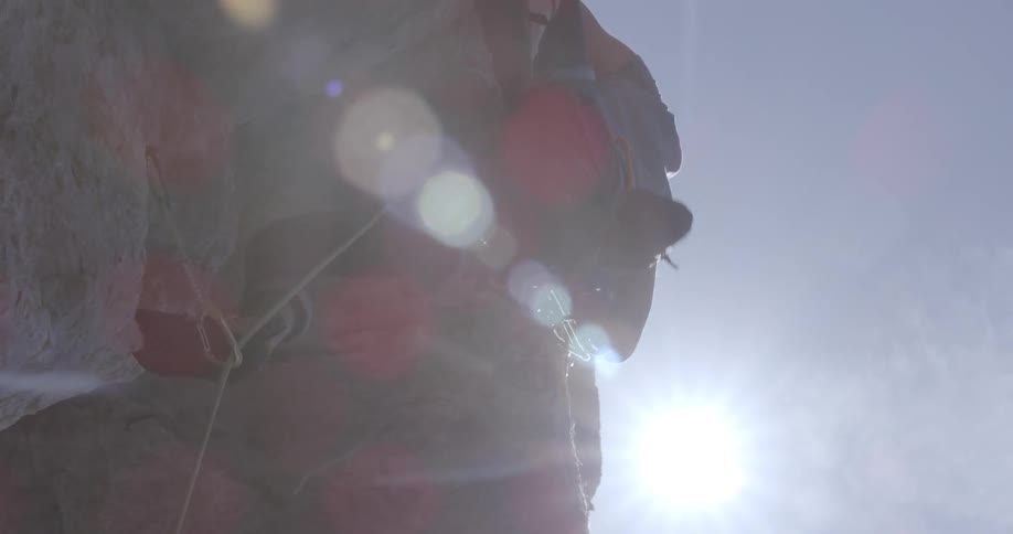 Sun shines over a man climbing a rock wall next to the ocean