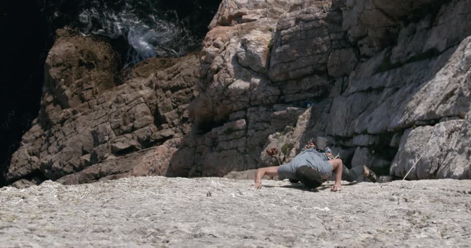 Man climbs a rock wall next to the ocean