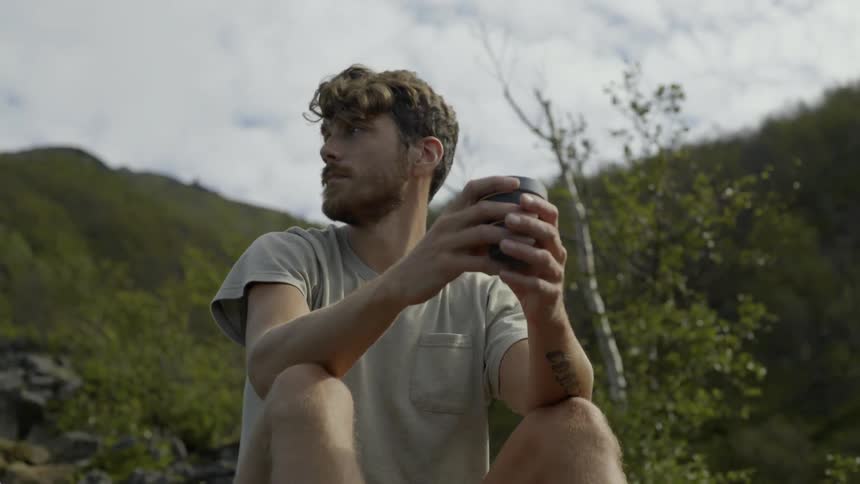 A thoughtful traveler looks out across a vast forest valley during his solo journey.