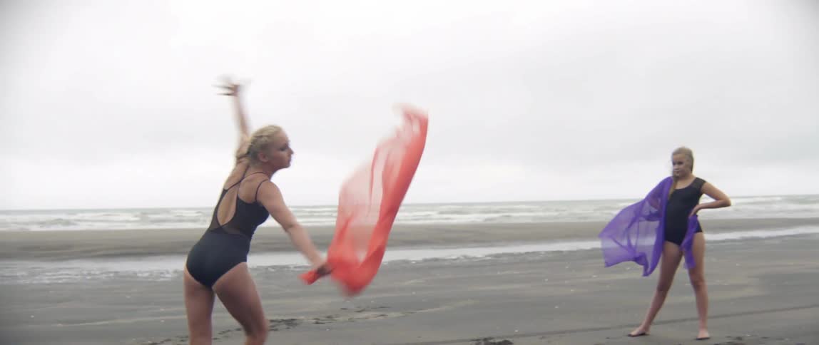 A girl does some gymnastics and dance moves on the beach as others watch