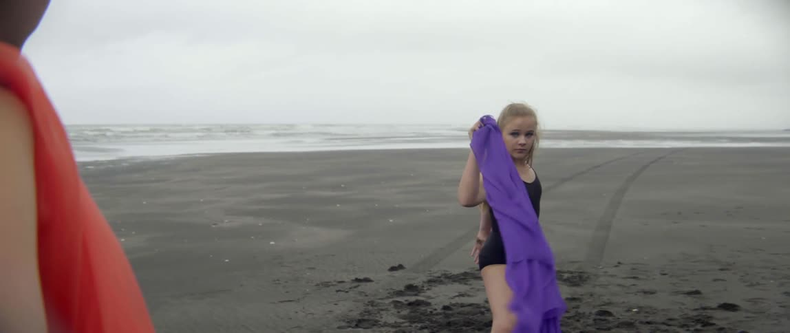 A girl holding a purple scarf throws it forward while holding it
