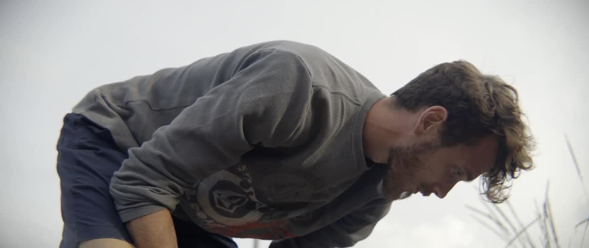 Man in shorts and a long sleeve shirt bends over a project he is working on