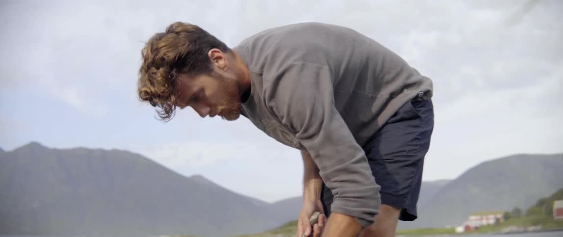 An adventurous hiker bends down to examine a curious object on the forest floor.