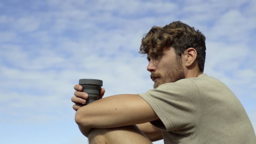 A melancholic young man processes complex emotions during a quiet outdoor mountain getaway.