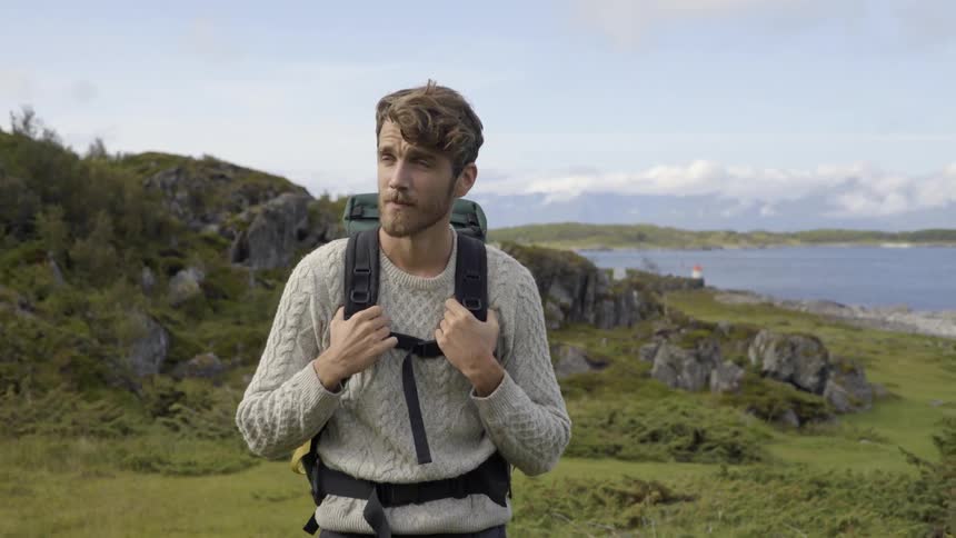 An ambitious traveler explores a remote island hill while carrying his camping equipment.